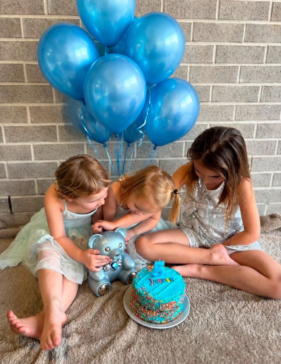 Jasper’s sisters with his blue teddy bear urn, blue balloons and a birthday cake